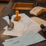 Mesa de escritório com documentos variados e carimbos sobre os papéis.