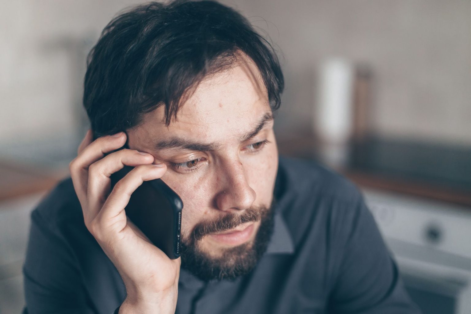Homem com expressão preocupada usa o celular sentado em um ambiente interno.