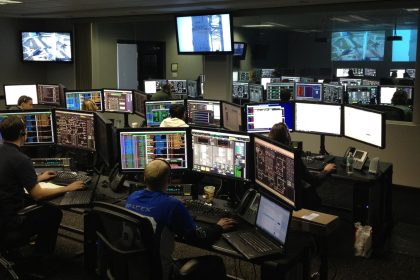 Profissionais trabalham diante de vários monitores em uma sala de controle.
